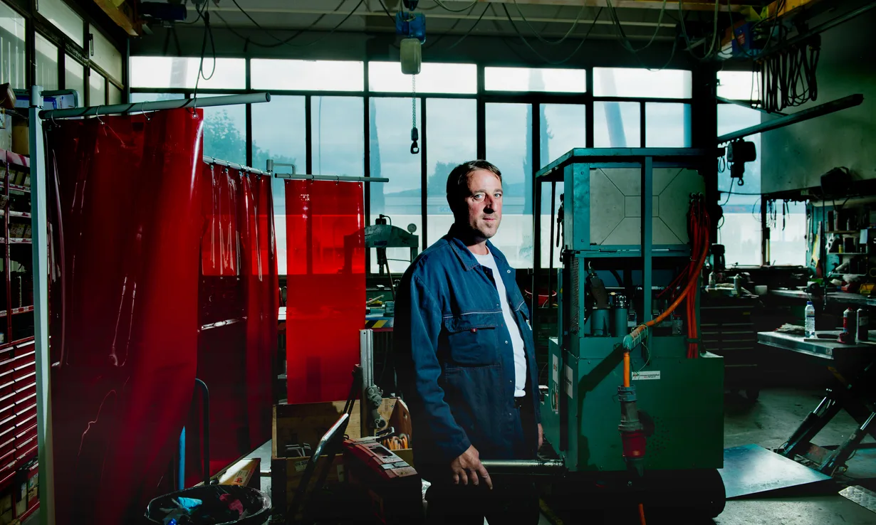 Artisan dans son atelier de métallerie, devant un rideau de soudure et des machines