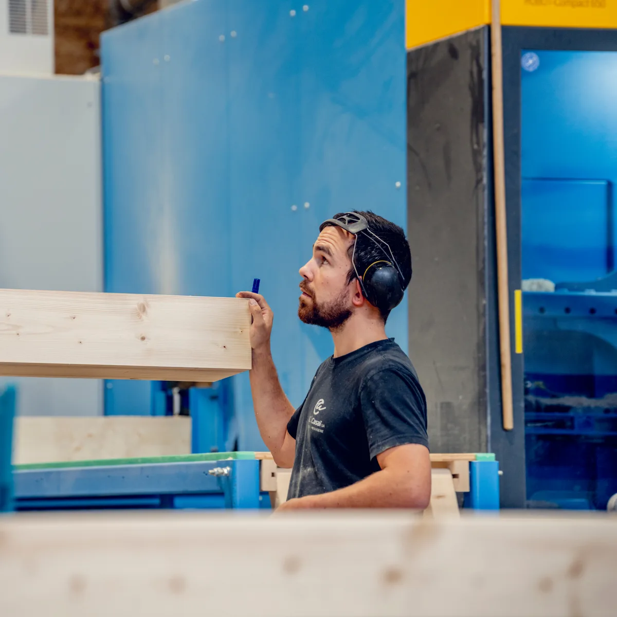 Ouvrier contrôlant une poutre en bois lamellé-collé dans un atelier de construction bois