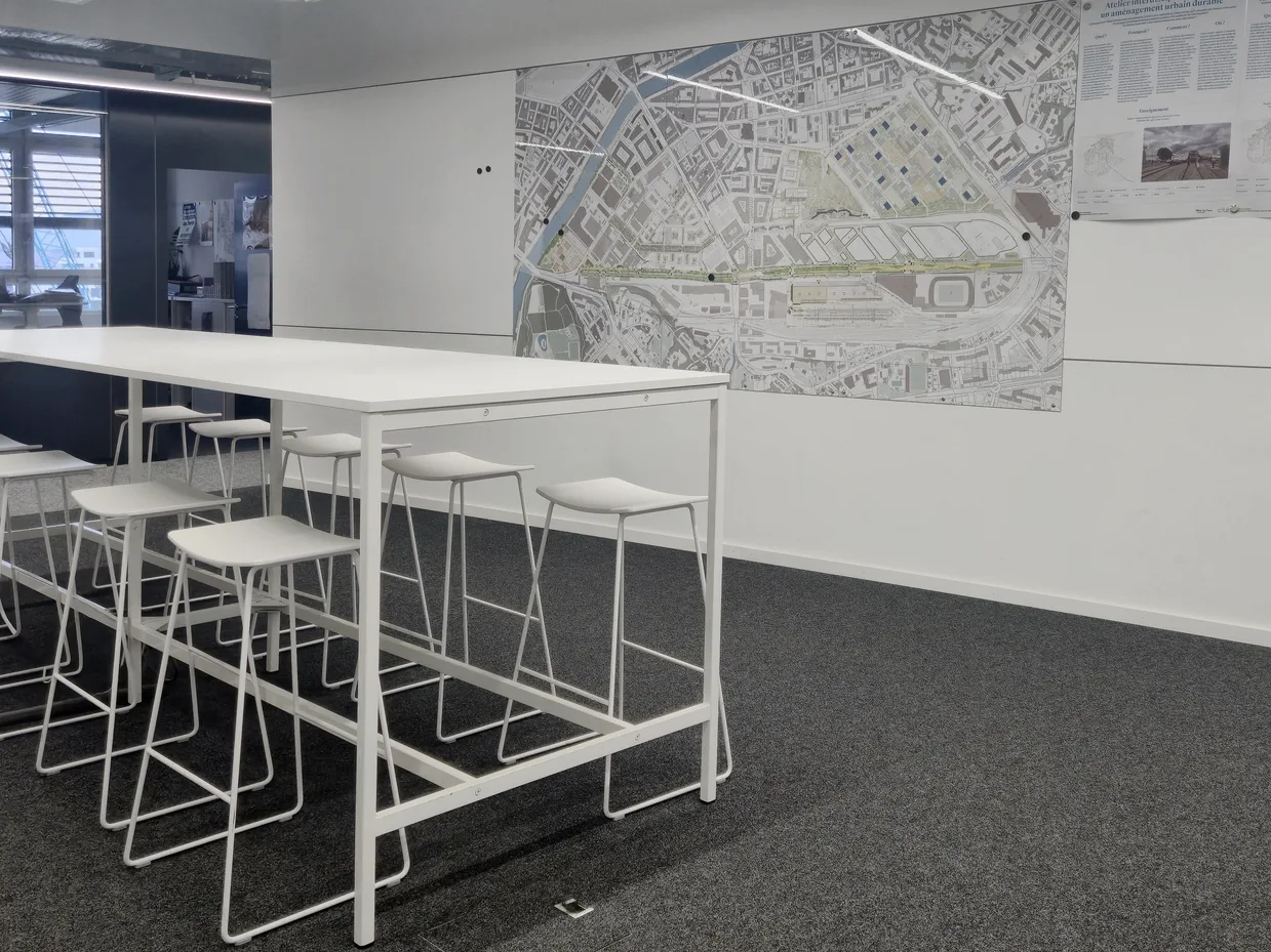 Espace de réunion informel avec tables hautes et un grand plan de la ville au mur, dans les bureaux de la FTI